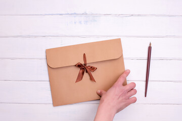 Hand holding Craft envelop and ink pencil   on white   wooden background
