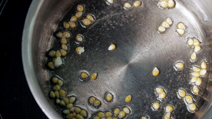 Yellow popcorn seeds exploding on a hot metal frying pan with oil.