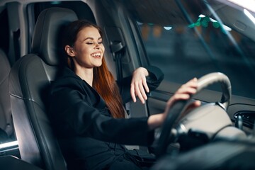 Obraz na płótnie Canvas a happy, relaxed woman enjoys a night ride at the wheel while sitting in a car and smiling broadly squints her eyes with happiness
