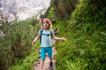 Cute girl walking along mountain trail descending into forest.