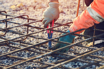 Builder's hands fixing steel reinforcement bars at construction site. Steel fixer assembling reinforcement cage. Selective focus - obrazy, fototapety, plakaty