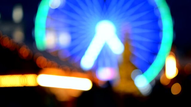 Ferris wheel decorated blue illumination, Christmas tree, black silhouettes of people walking, city buildings at winter night. Christmas Town. Beautiful New Year Christmas holiday blurred background