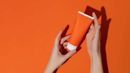 Female hands holding blank orange plastic cosmetic tube on orange background.Mockup