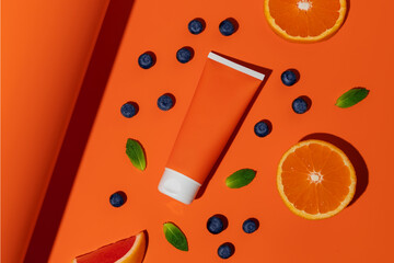 Blank plastic bottle of sun protection with fruit on orange background. Mockup of sunscreen cream.