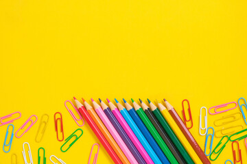 Colored pencils and paper clips yellow background.