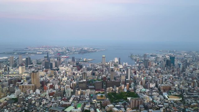 Day to night aerial time lapse over downtown Kobe as ferry departs port