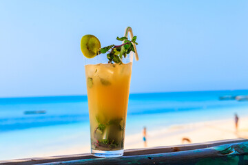 Glass of fresh orange mojito cocktail by the ocean