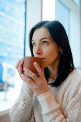 Portrait of a young woman in white sweter with a cup of coffee in hand   while at cafe