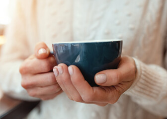 Portrait of a young woman in white sweter with a cup of coffee in hand   while at cafe Cold handds worm coffee