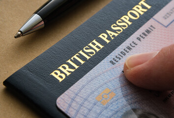 Finger pointing at Biometric Residence permit Card (ILR, Indefinite leave to Remain) placed on top of British passport. Concept for naturalization. Stafford, United Kingdom, July 20, 2022 - obrazy, fototapety, plakaty