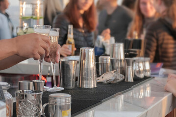 Closeup of a bartender's hands pouring couple of champagne glasses in bar.