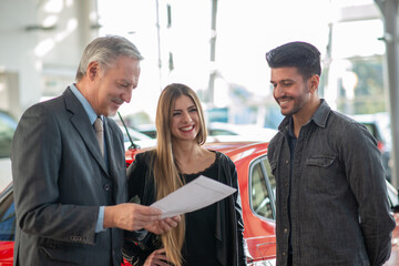 Family talking to the salesman and choosing their new car in a showroom