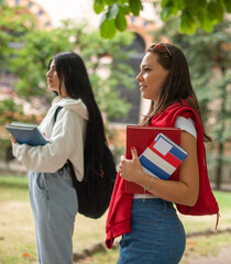 Student holding a book while walking outdoor in the park and smiling