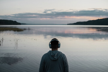 A man listens to music with headphones, looks at the lake, balance and harmony of the soul