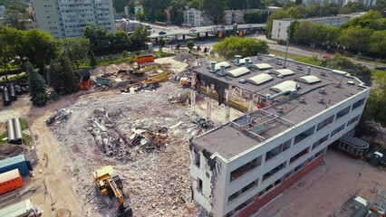 A three-storey building being taken down by a yellow digger. Horizontal aerial shot of a damaged...