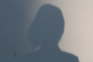 A silhouette of the head of a woman. It is her shadow on a white wall.