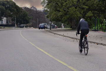 Cyclist tourist helmet rides on a long asphalt road in the steppes of Kazakhstan. On the trunk of a tourist backpack. Dry grass on the roadsides and blue sky in Mangystau.