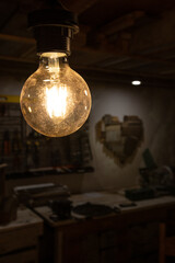 A close up of a light bulb hanging in an urban surrounding with in the background a wooden heart on the wall