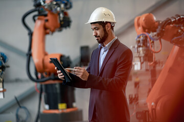 Automation engineer uses tablet for programming robotic arm in factory.