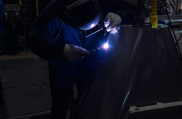 Skillful welders weld stainless steel in the factory. Construction site metal welder. builder wear fireproof gloves for safety at work.
