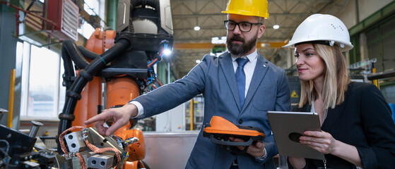 Chief engineer and project manager in modern industrial factory with robot arms talking and...
