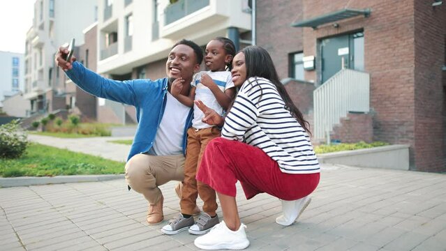 Cute stylish African American family with little child taking selfie photo outdoor using smartphone. Small boy taking pictures with happy parents on cellphone camera on street. Childhood concept