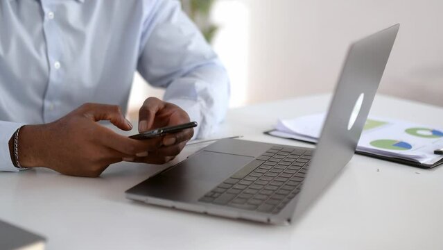Close-up view of male hands typing on smartphone keyboard. Caucasian businessman using mobile phone and laptop while working online in modern office, browsing internet, texting online, typing text