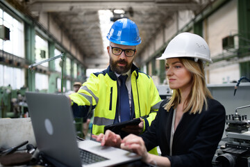 Male and female industrial engineers discussing factory's new machinery project and using laptop.