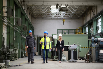 Manager supervisors and industrial worker in uniform walking in large metal factory hall and...