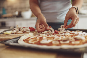 A woman spreads mushrooms on a homemade pizza before baking in the oven