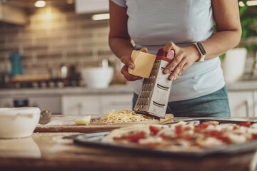 Women's hands rub cheese for pizza ready for baking in the background of the kitchen