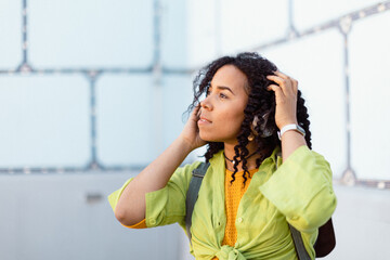 Young biracial woman wearing headphones and enjoying listening to music outdoors in street. - Powered by Adobe