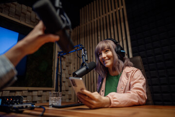 Young woman host talking to microphone and interviewing a man for a radio podcast.