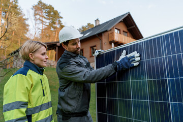 Handyman solar installer discussing with his colleague at solar module in front of family house.