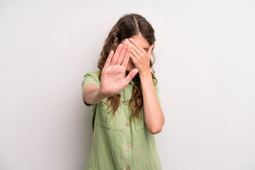 young adult pretty woman covering face with hand and putting other hand up front to stop camera,...