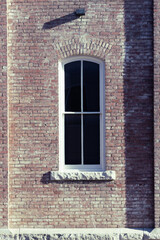 Close up of old window with white grilles and stone sill on old brick building, vintage aged building