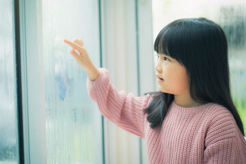 Girl writes finger at wet glass touching wet window. Children's hand writes on a wet window.