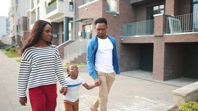 African American young cheerful lovely family on a walk in the city. Beautiful mother and handsome father walking together with little son child holding hands and talking. Leisure, childhood concept