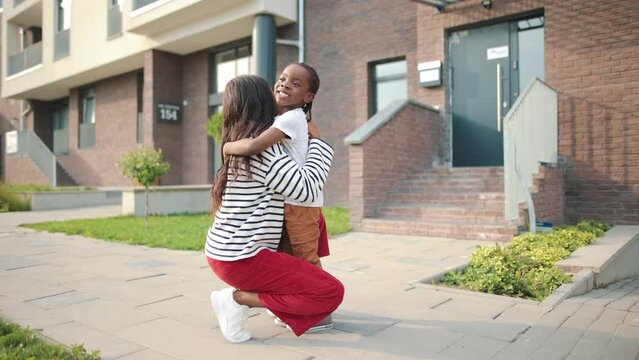 Side view of young beautiful African American mom speaking with little cute son embracing him outdoors in town. Caring mother on a walk hugging child boy on street, family, love, childhood concept