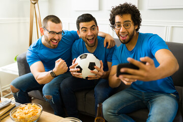 Excited friends taking a selfie while hanging out to watch a soccer game on tv