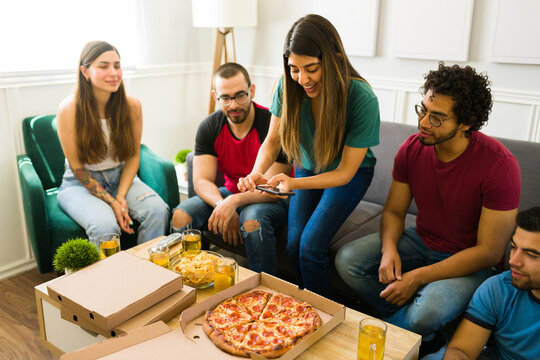 Young woman taking a photo while eating pizza with friends