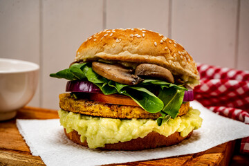 Vegan veggie protein burger, with tomato, arugula, red onion, mushrooms and avocado mayonnaise on a wooden board and a white background. Normal view.