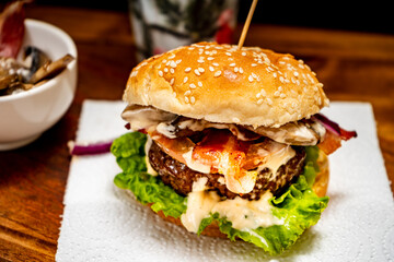 Homemade beef burger with lettuce, tomato, mushrooms and cheese on a wooden board with black background. Chopped view. Copy text. Fastfood concept.