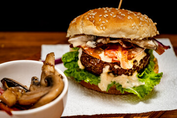 Homemade beef burger with lettuce, tomato, mushrooms and cheese on a wooden board with black background. Chopped view. Copy text. Fastfood concept.