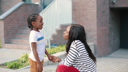 Close up of happy African American little cute boy talking with beautiful young mother on street. Side view of woman parent having conversation with joyful kid outside. Leisure, family time concept