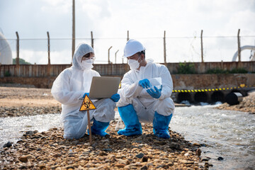 Ecologist sampling taken dead fish to inspaction and save data to laptop computer, Biologist wear protective suit and mask collects sample of waste water from industry, problem environment