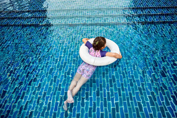 Happy Asian little girl enjoys swimming in outdoor swimming pool on hot summer day.