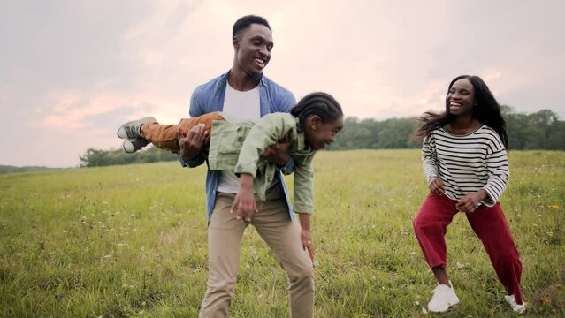 African American young family mom and dad playing with cute kid in green field and smiling laughing having fun. Parents play with little son on meadow spending day out together, love and care