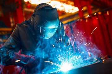 Laborer in protective mask welds manually metal frame - obrazy, fototapety, plakaty