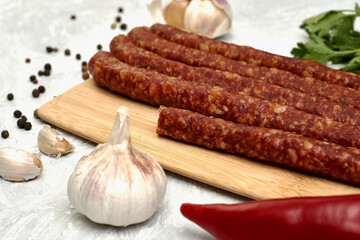 spicy smoked sausages on a cutting board next to red pepper garlic spices and herbs on the table